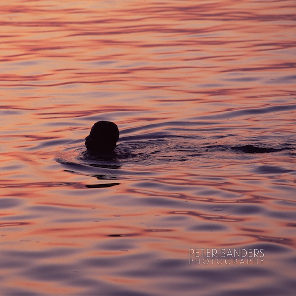 Young boy swimming close to the jetty in the sunset.